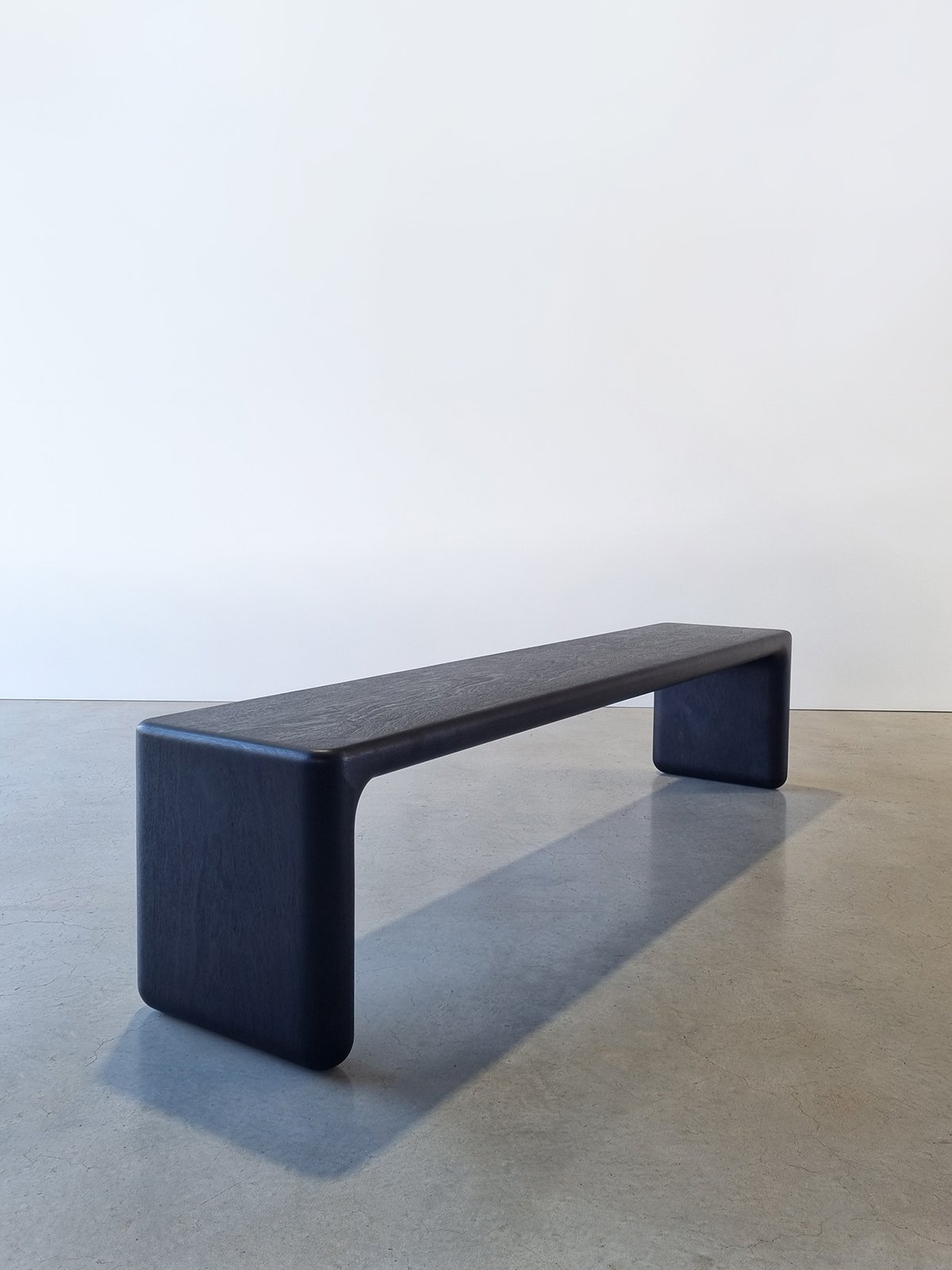 Elongated Hippo Bench in Ebonised Jarrah with rounded waterfall legs and a subtly textured surface, plain studio setting - bespoke seating by Nathan Day Design