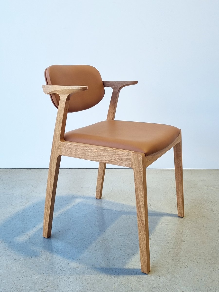 Kinross Chair in Blackbutt with tan leather upholstered seat and back, classic mid-century aesthetic, blue studio backdrop - bespoke dining chair by Nathan Day Design