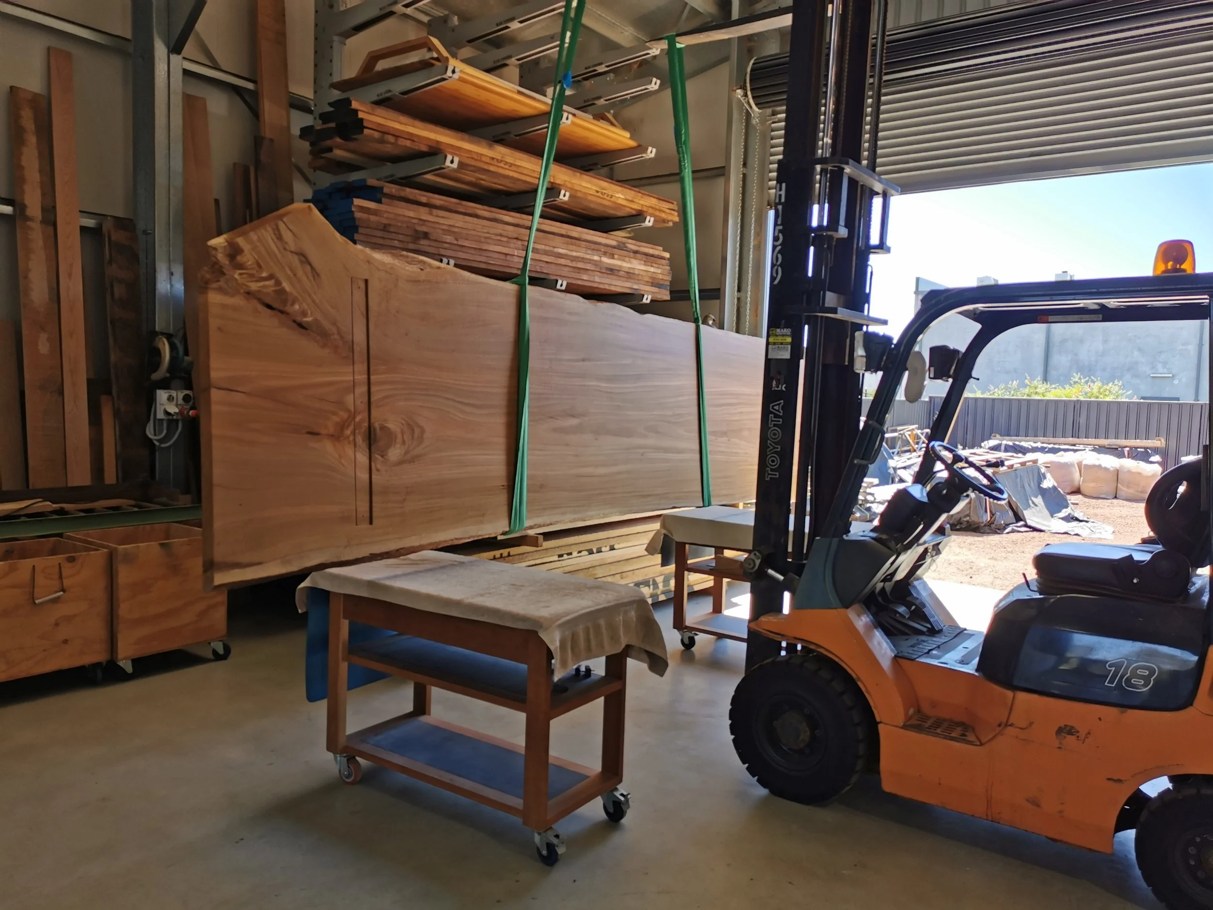 Raw timber slab being moved into the workshop by forklift and lifting straps for the live edge table process - Nathan Day Design