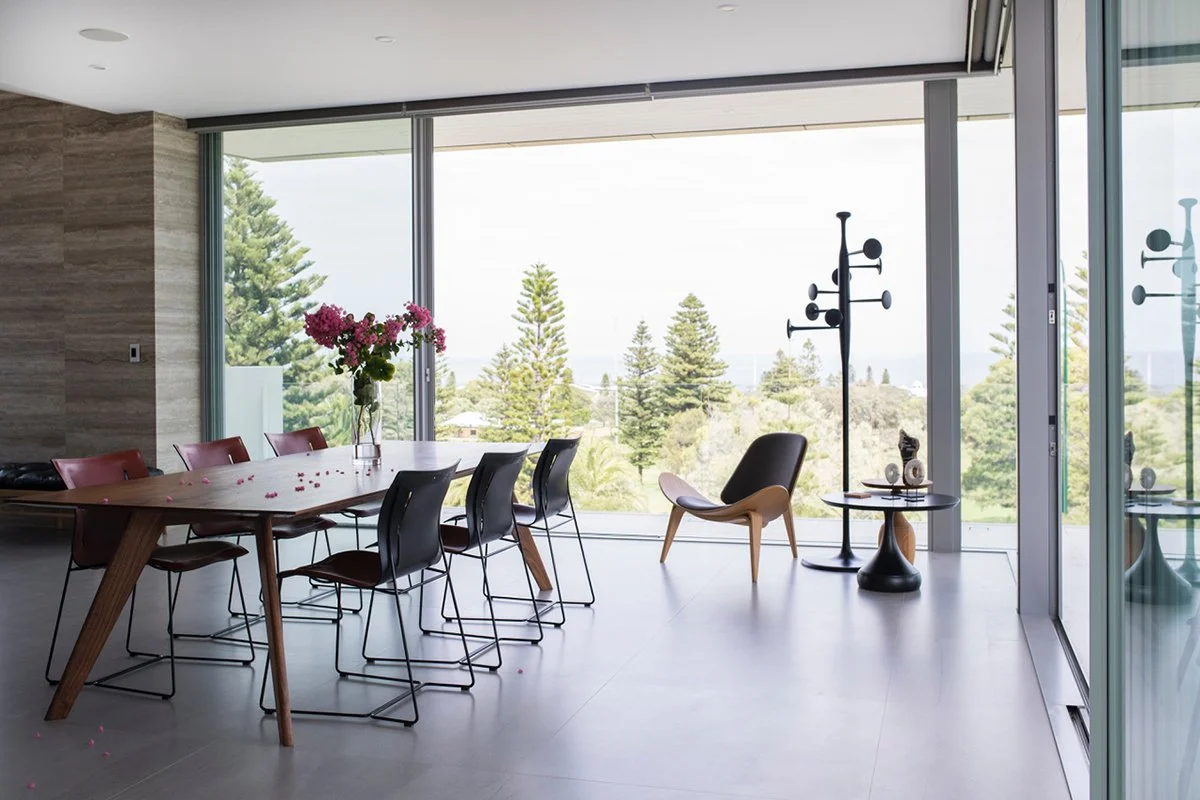 Vista St Table in Walnut styled in a coastal home with floor-to-ceiling glass and ocean view, black dining chairs - bespoke furniture by Nathan Day Design