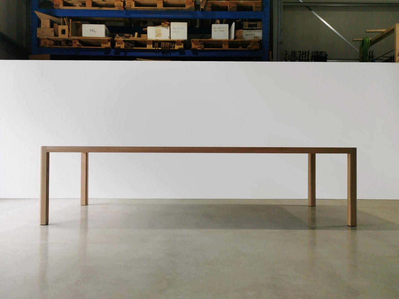 Irvine Table torsion box dining table in American Walnut, shown front-on in workshop setting with pallet racking backdrop - bespoke furniture by Nathan Day Design
