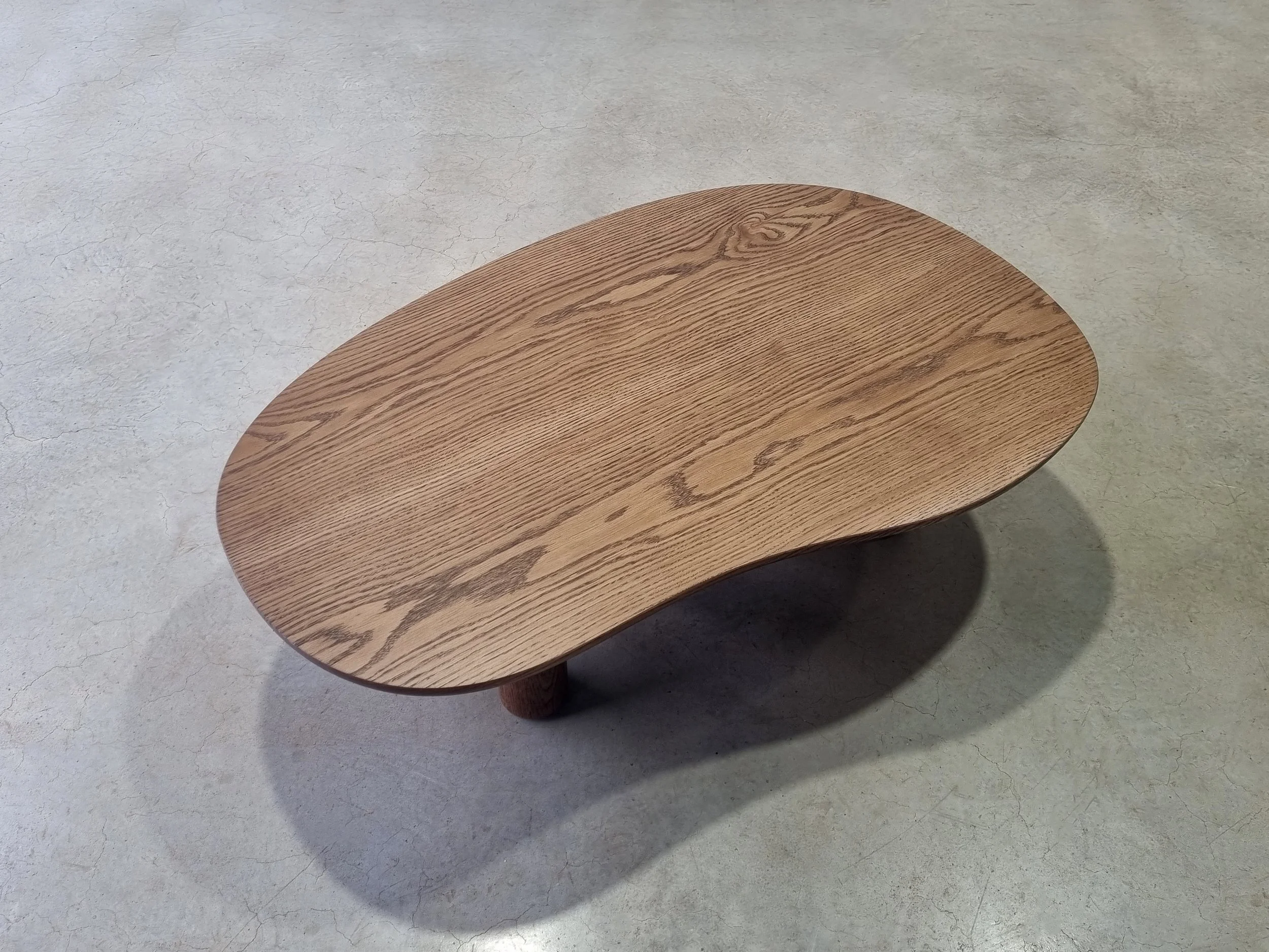 Overhead view of the Anemone coffee table's organic curved silhouette in tinted American Oak, showing rich grain - Nathan Day Design