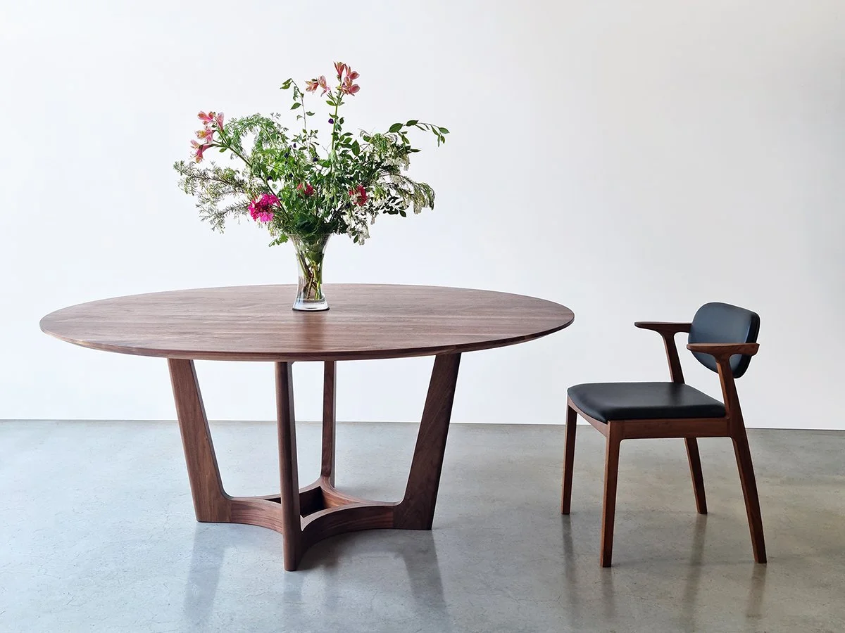 Round Froxfield Table in Walnut with the signature curved base, styled with a floral arrangement - Nathan Day Design
