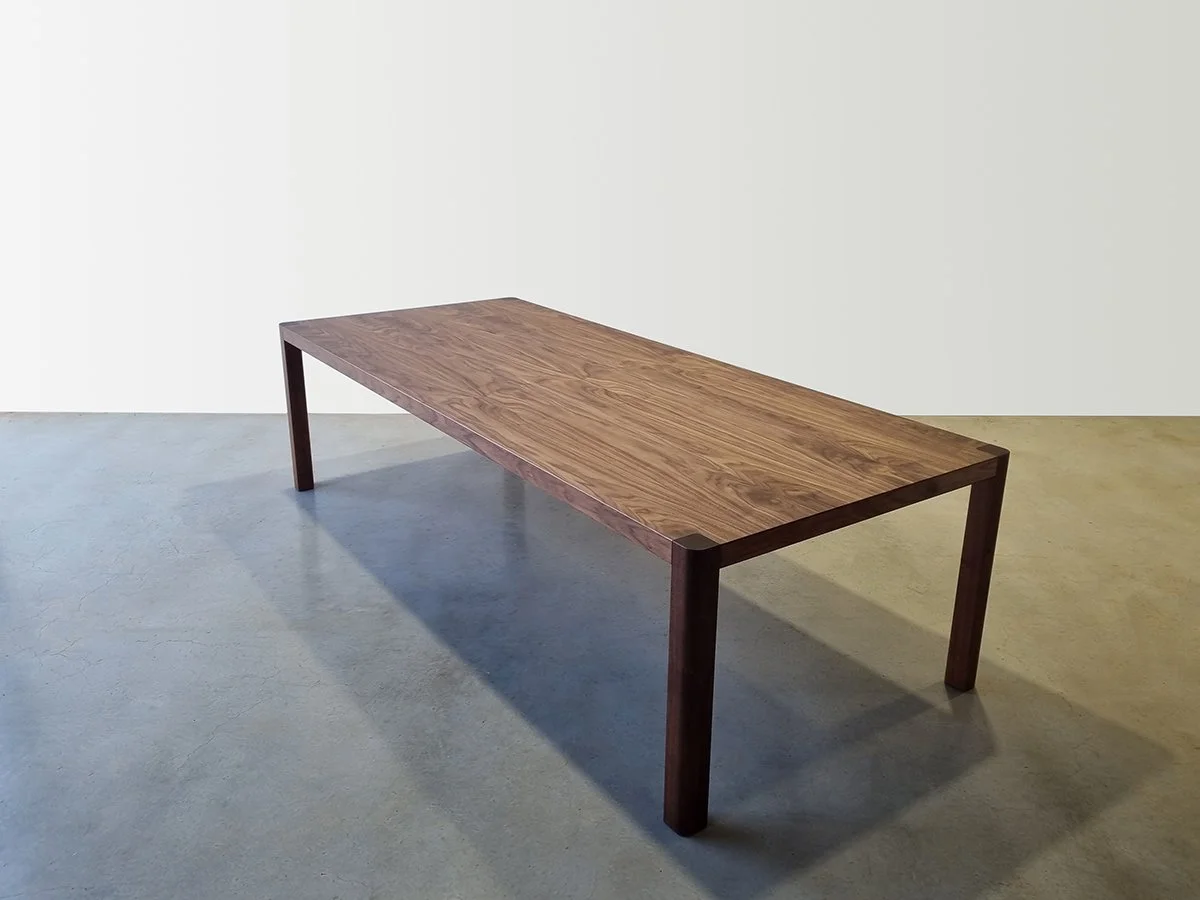 Angled full-length view of Irvine Table torsion box dining table in American Walnut, plain studio setting - bespoke furniture by Nathan Day Design