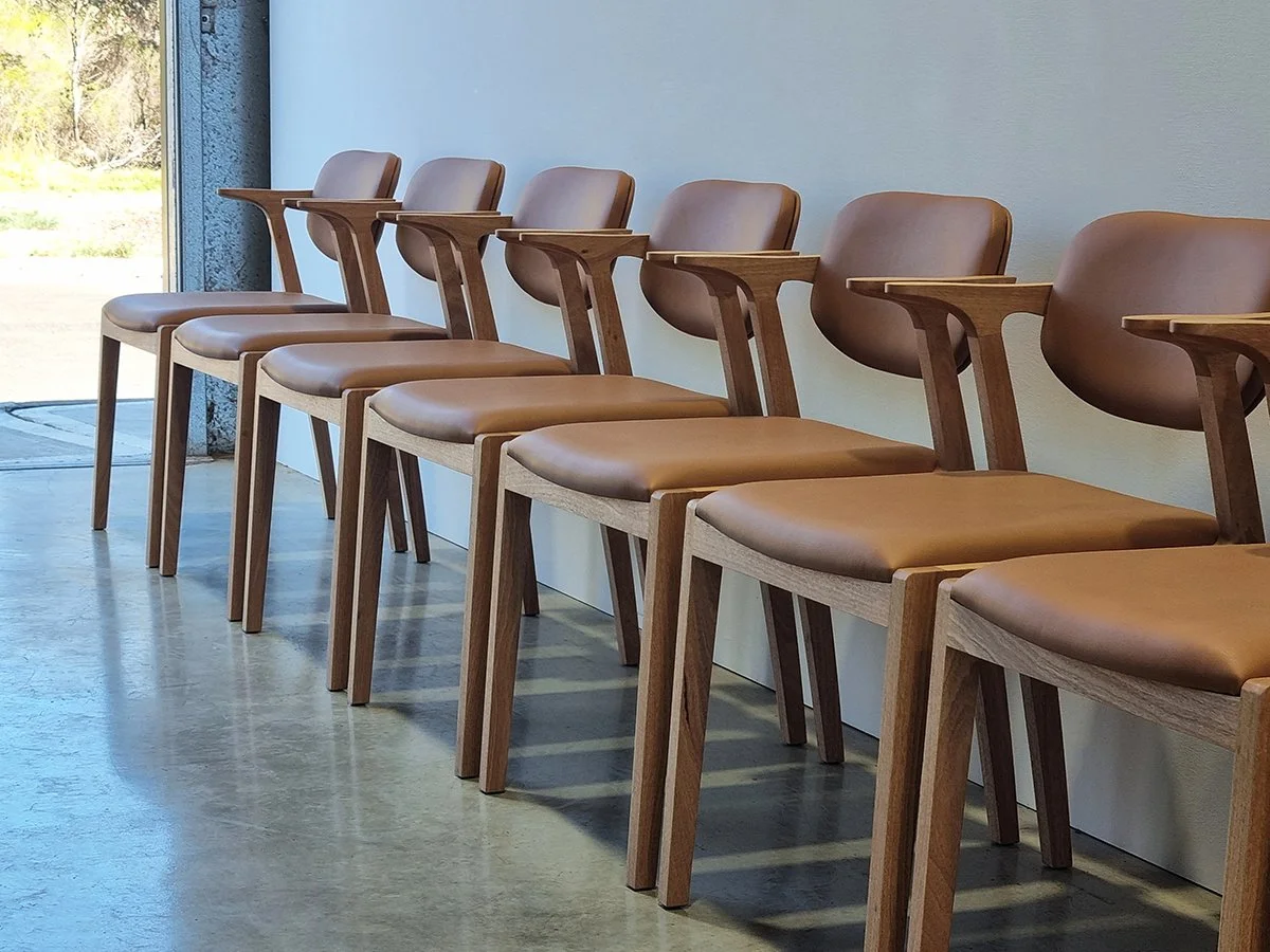 Row of Kinross Chairs in tan leather and American Oak lined up along the workshop wall near the doorway - bespoke furniture by Nathan Day Design