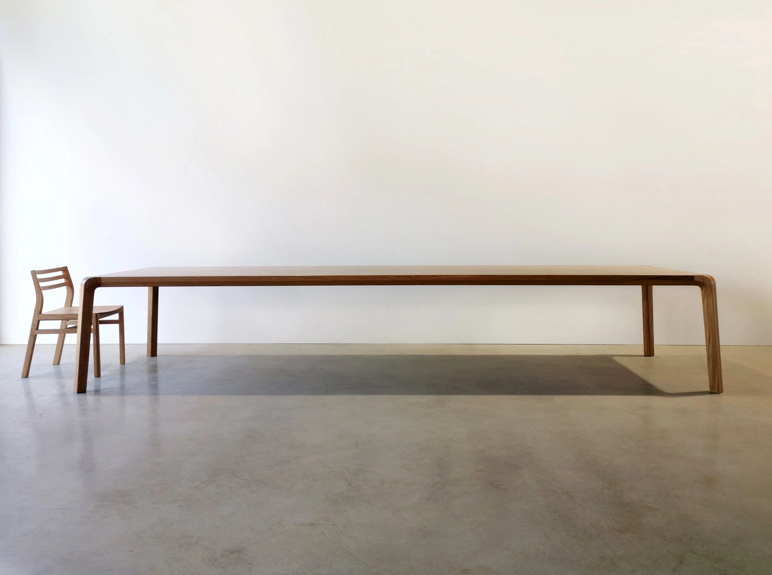 Long waterfall-edge bench in Walnut shown with a Walter Dining Chair for scale, plain studio setting - Nathan Day Design