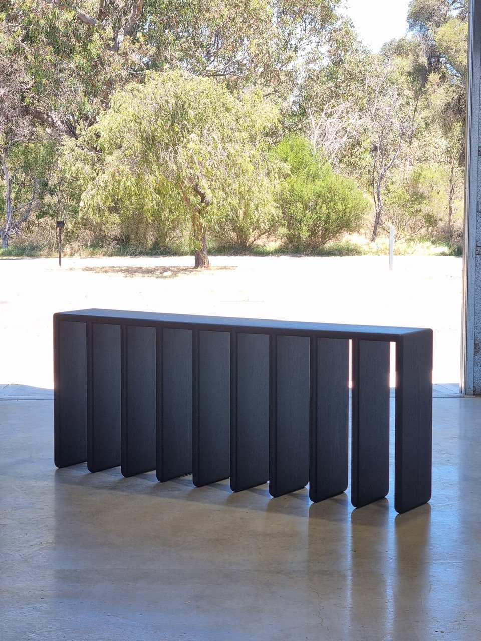 Millipede Console in ebonised Jarrah, outdoor lifestyle setting with bushland backdrop - Nathan Day Design