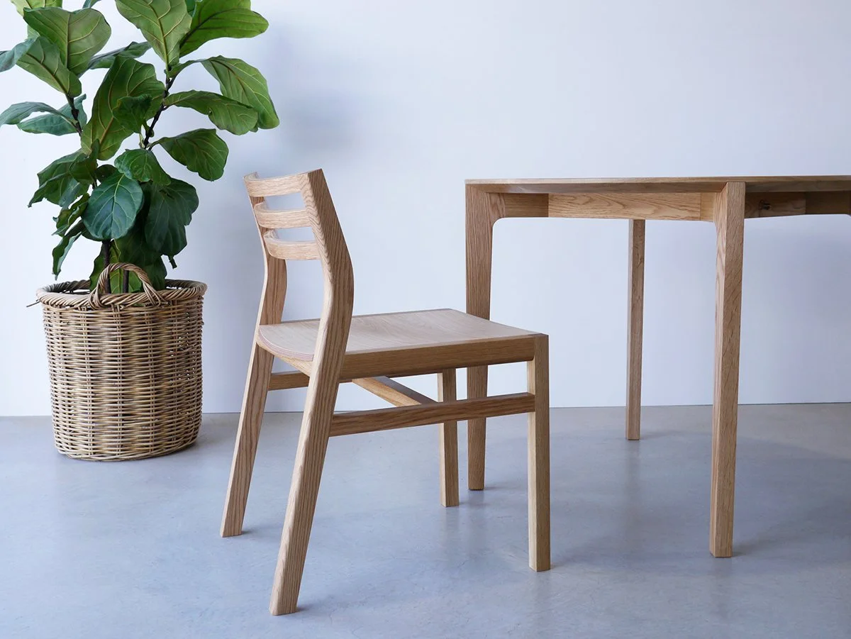 Walter Dining Chair in American Oak beside a matching dining table and potted plant, plain studio setting - bespoke furniture by Nathan Day Design
