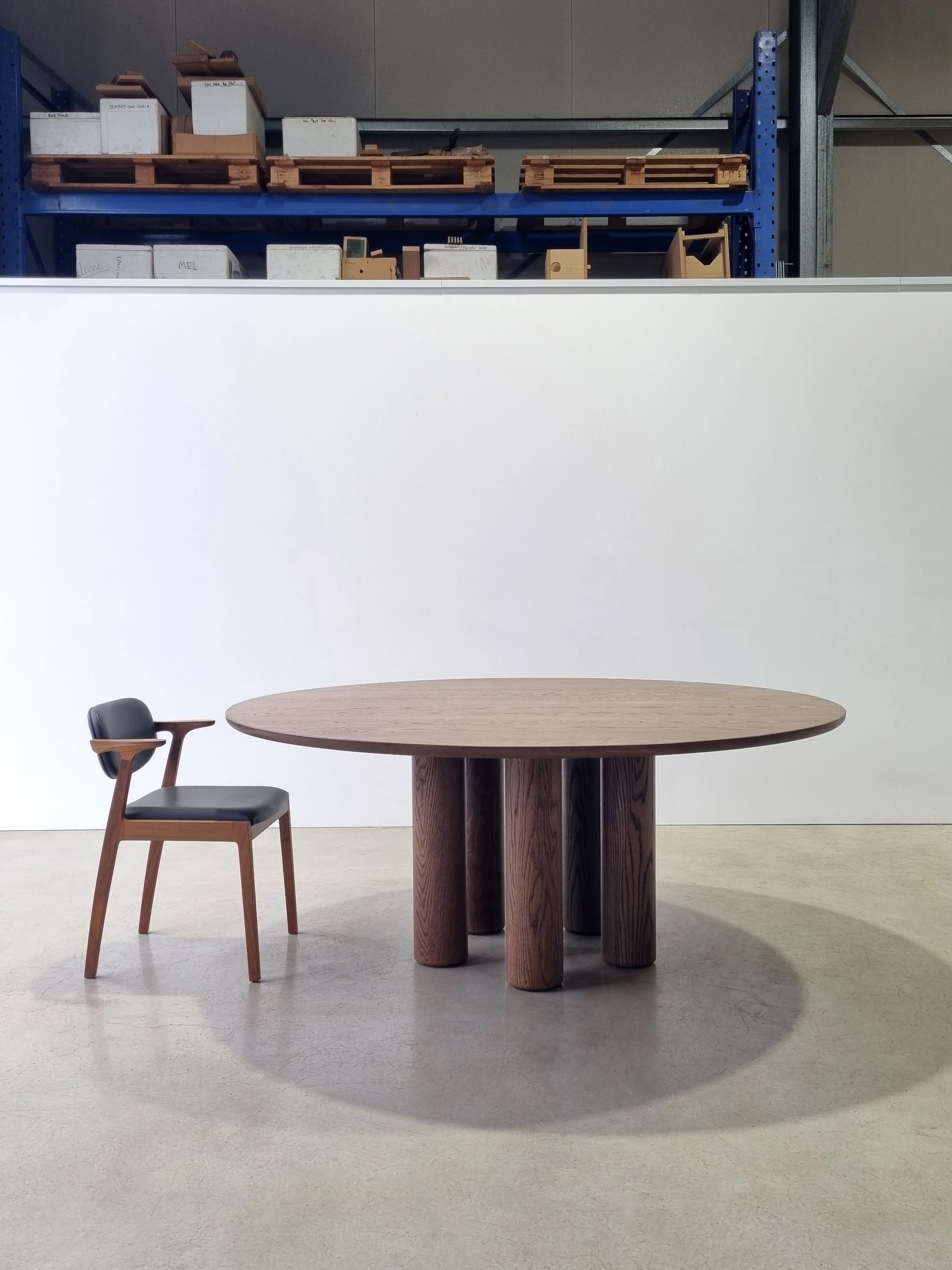 Anemone Table, a round dining table in tinted American Oak with strategically arranged column legs, paired with a dark timber dining chair - bespoke furniture by Nathan Day Design