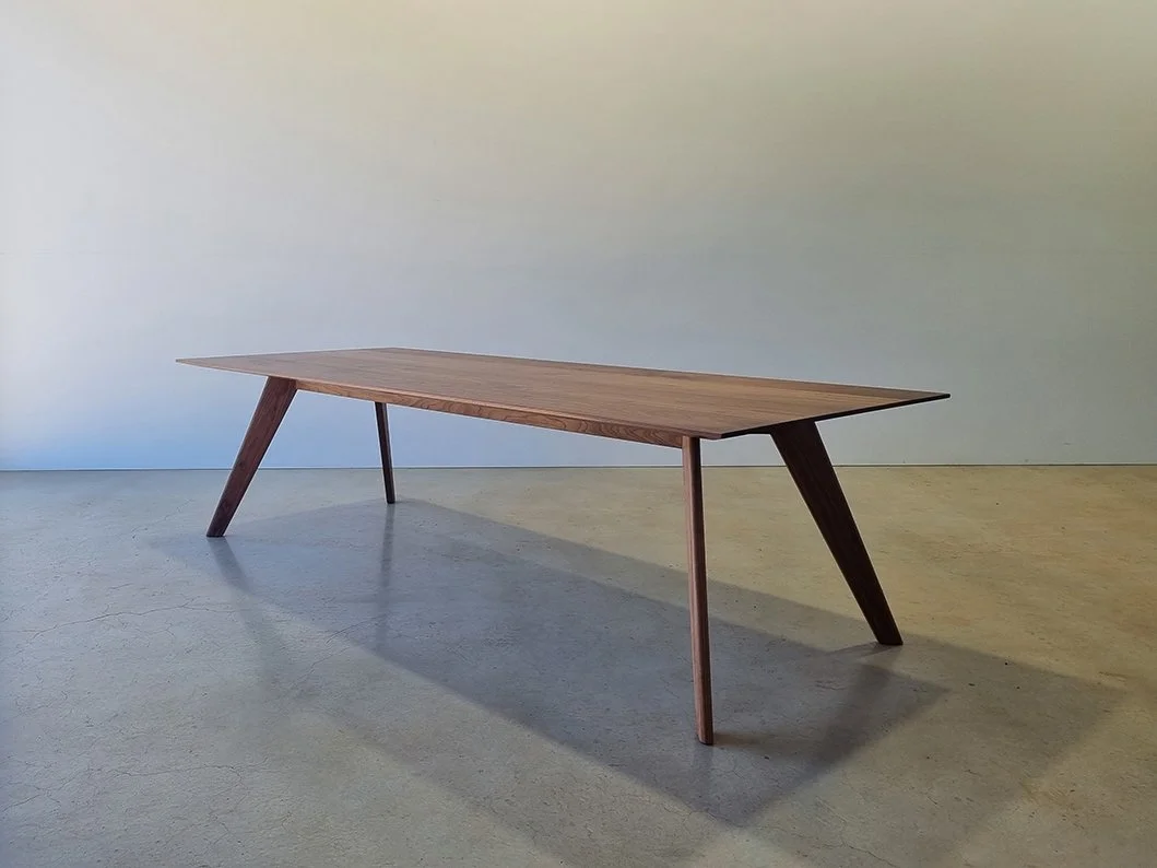 Angled full-length view of Vista St Table in Walnut with slender splayed legs, workshop setting - bespoke furniture by Nathan Day Design