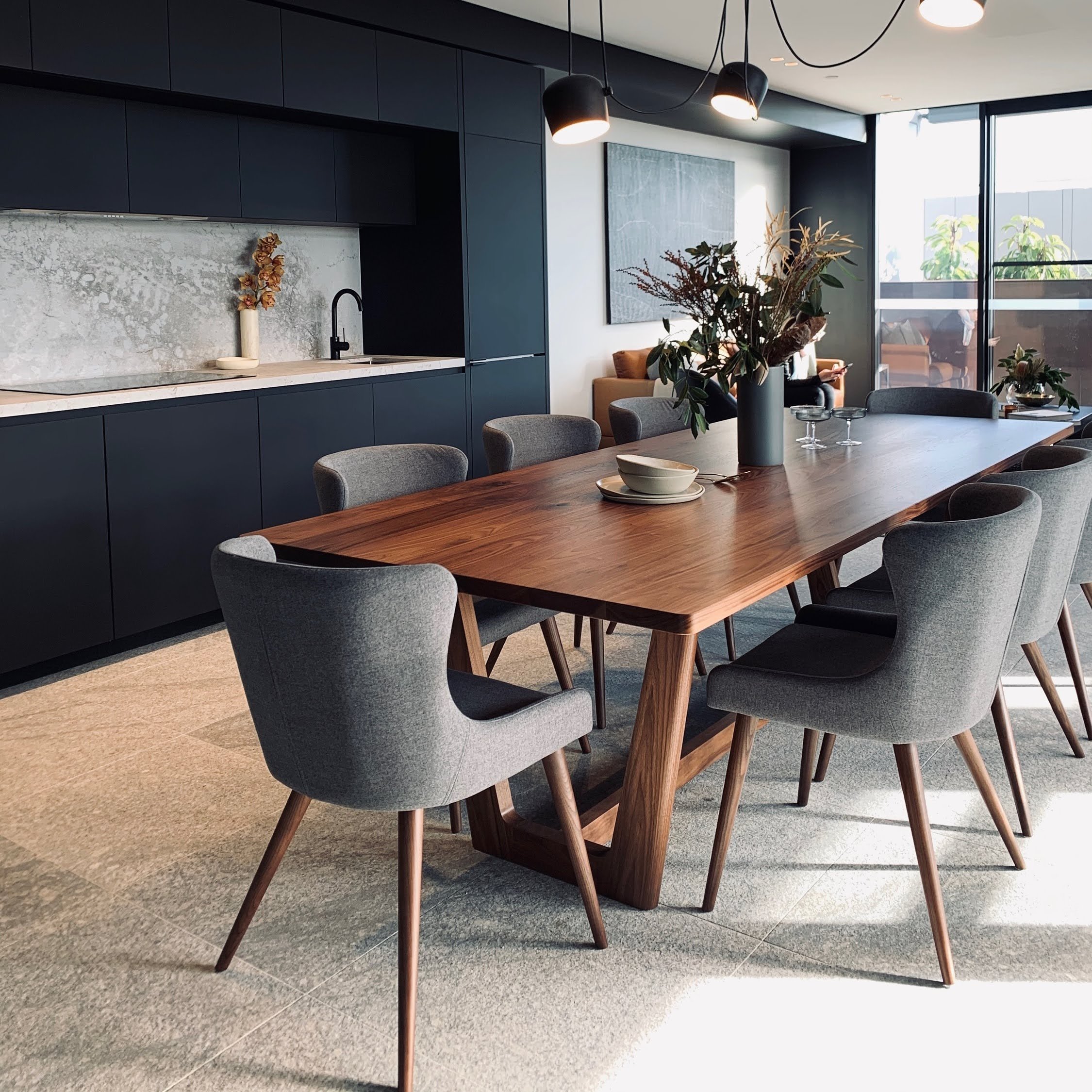 Botanical Table in Walnut styled in a dark kitchen interior with charcoal upholstered dining chairs and pendant lighting - bespoke furniture by Nathan Day Design