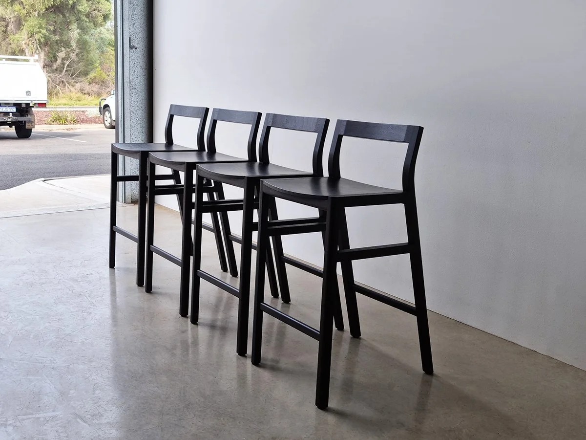 Low-back Bar Stools in ebonised Jarrah, row installed near entryway with concrete flooring - Nathan Day Design