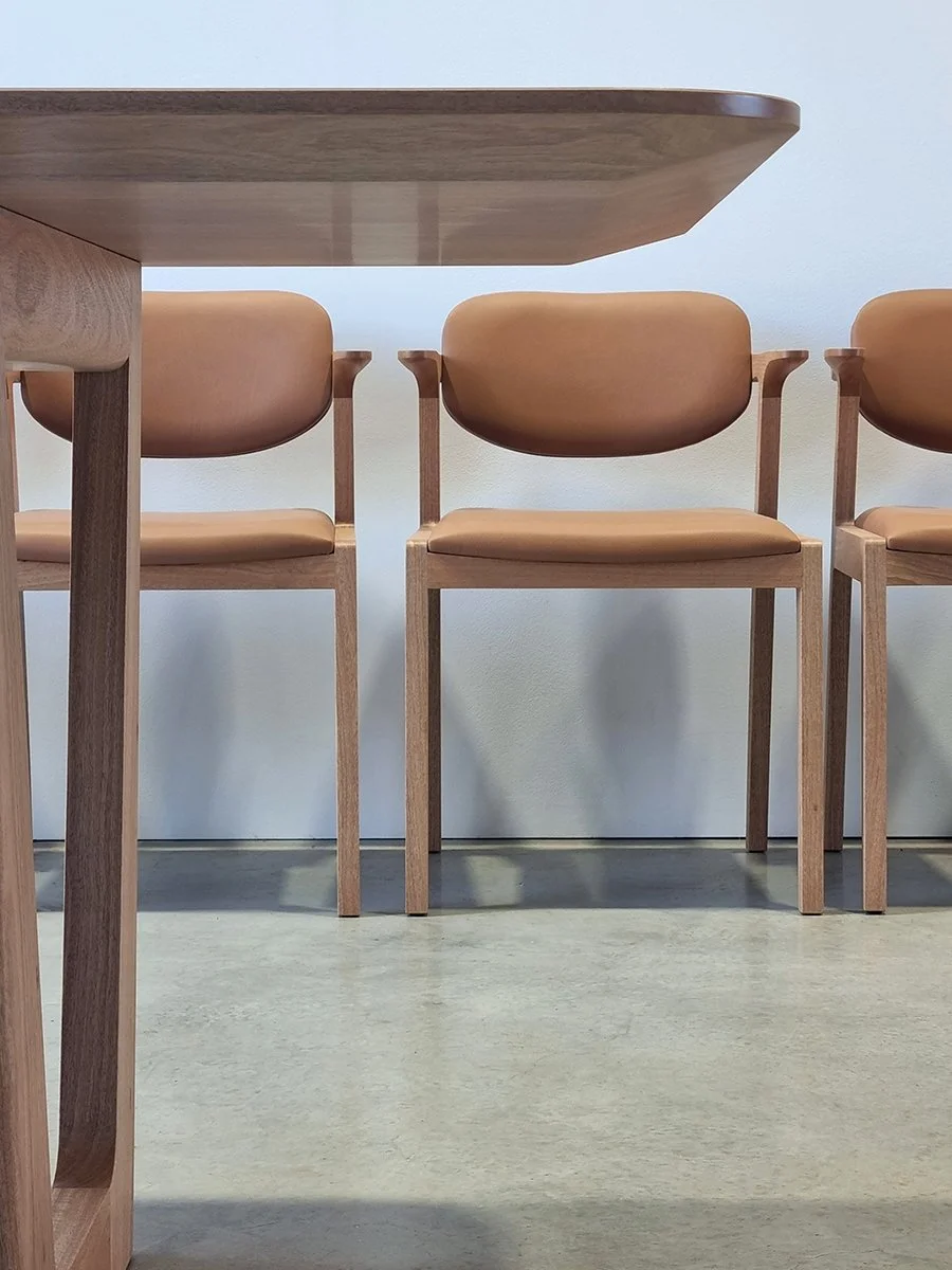 Low-angle view of Kinross Chairs in tan leather and Oak beneath a Walnut dining table edge, workshop setting - bespoke furniture by Nathan Day Design
