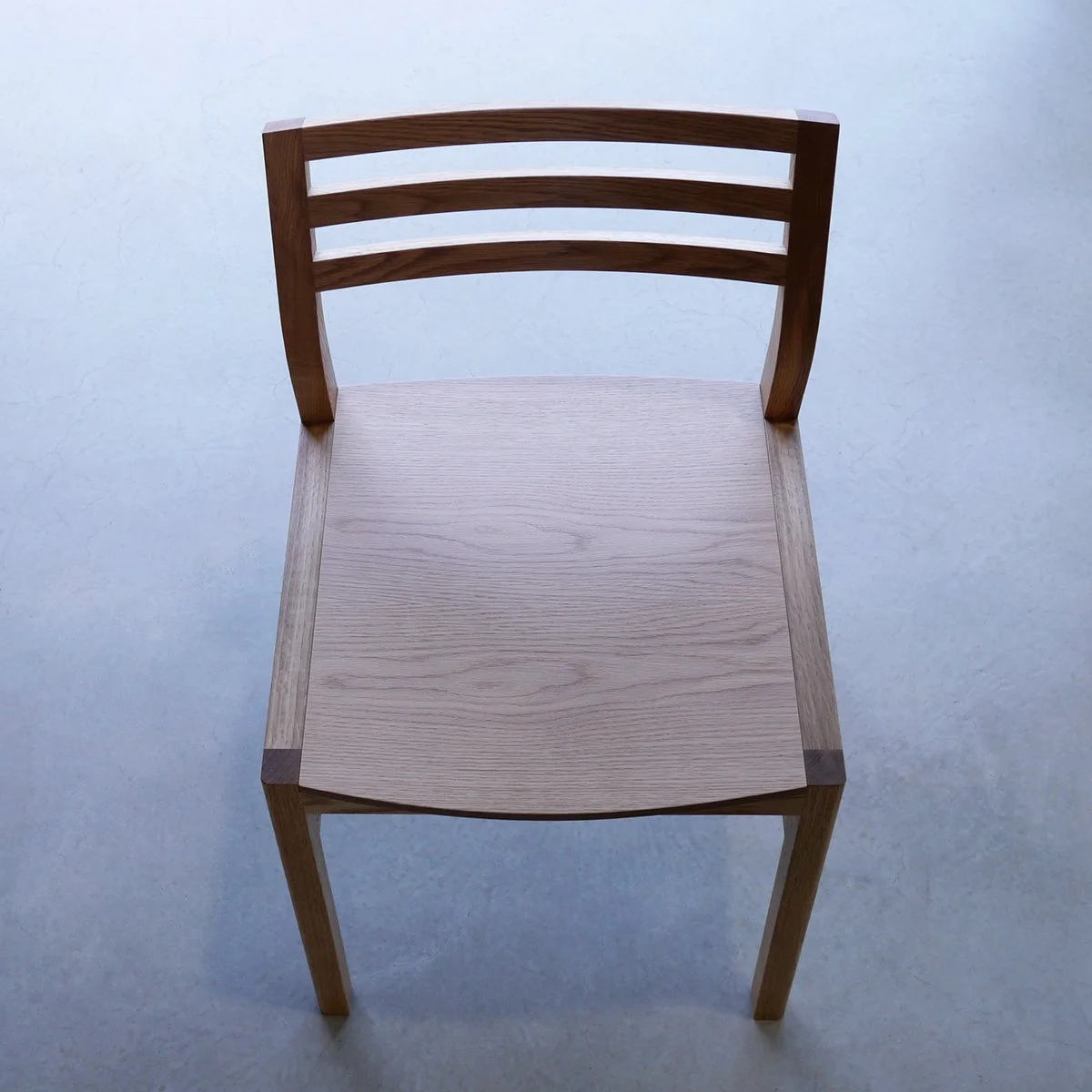 Walter Dining Chair in Walnut frame with contrasting lighter timber seat, front-on view in plain studio setting - bespoke furniture by Nathan Day Design