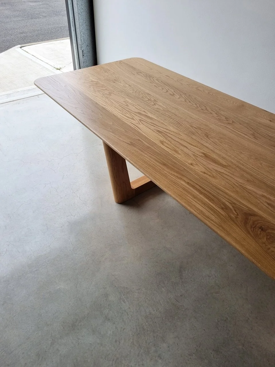Angled view of Aalia Table showing rounded corner leg and tabletop in American Oak, near workshop doorway - bespoke furniture by Nathan Day Design