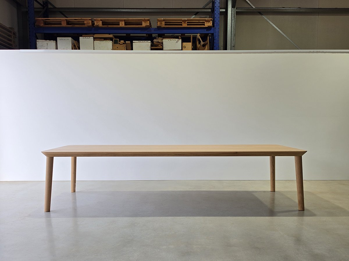 Mercator Way Table in American Oak, minimalist torsion box design shown head-on in workshop setting with pallet racking backdrop - bespoke furniture by Nathan Day Design