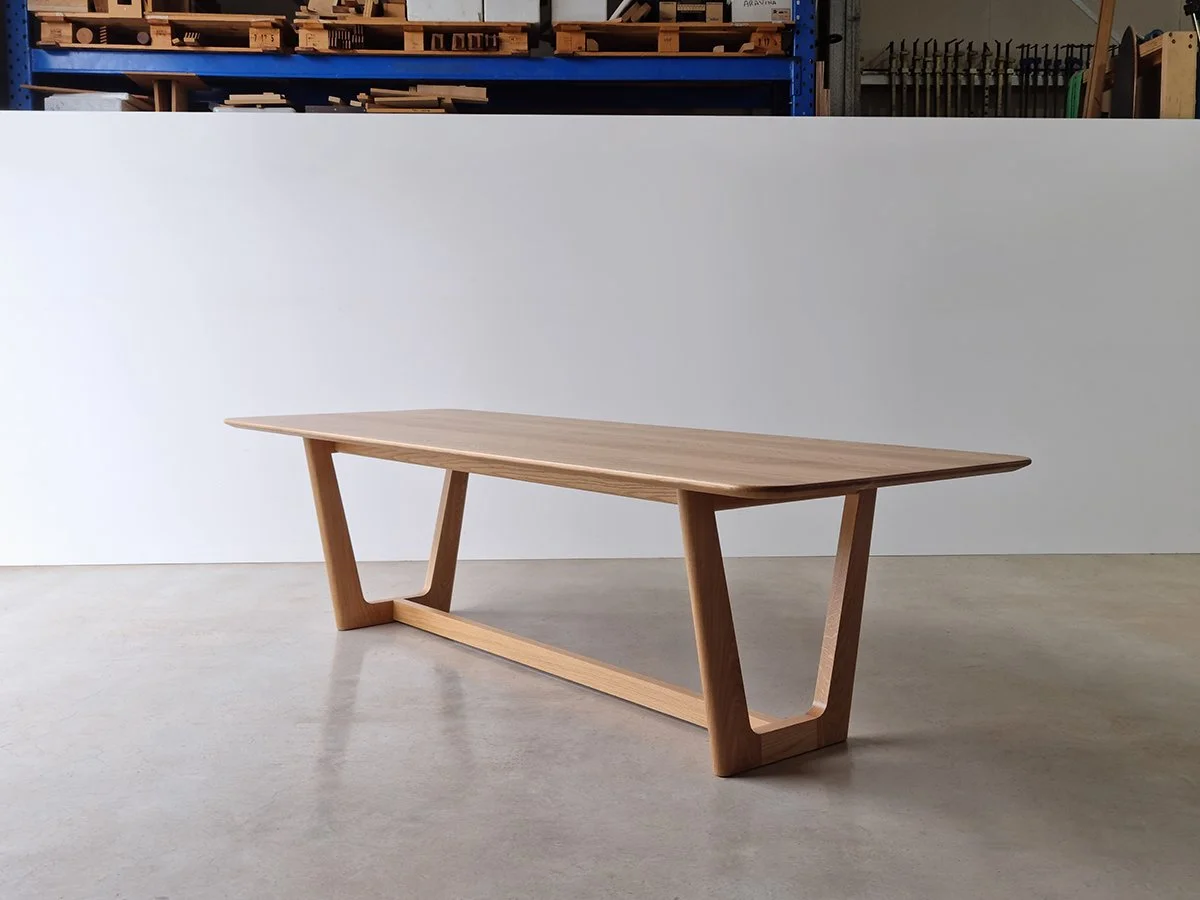 Botanical Table in Walnut with angled trestle base, shown front-on in workshop setting with pallet racking backdrop - bespoke dining table by Nathan Day Design