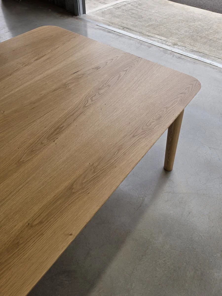Three-quarter angle view of Mercator Way Table in American Oak showing full length and tapered leg detail, workshop setting - bespoke furniture by Nathan Day Design