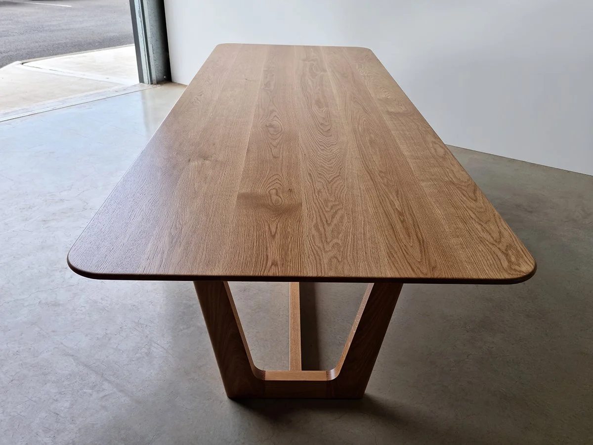 Elevated view of Botanical Table tabletop grain and angled trestle base in American Oak, near workshop roller door - bespoke furniture by Nathan Day Design