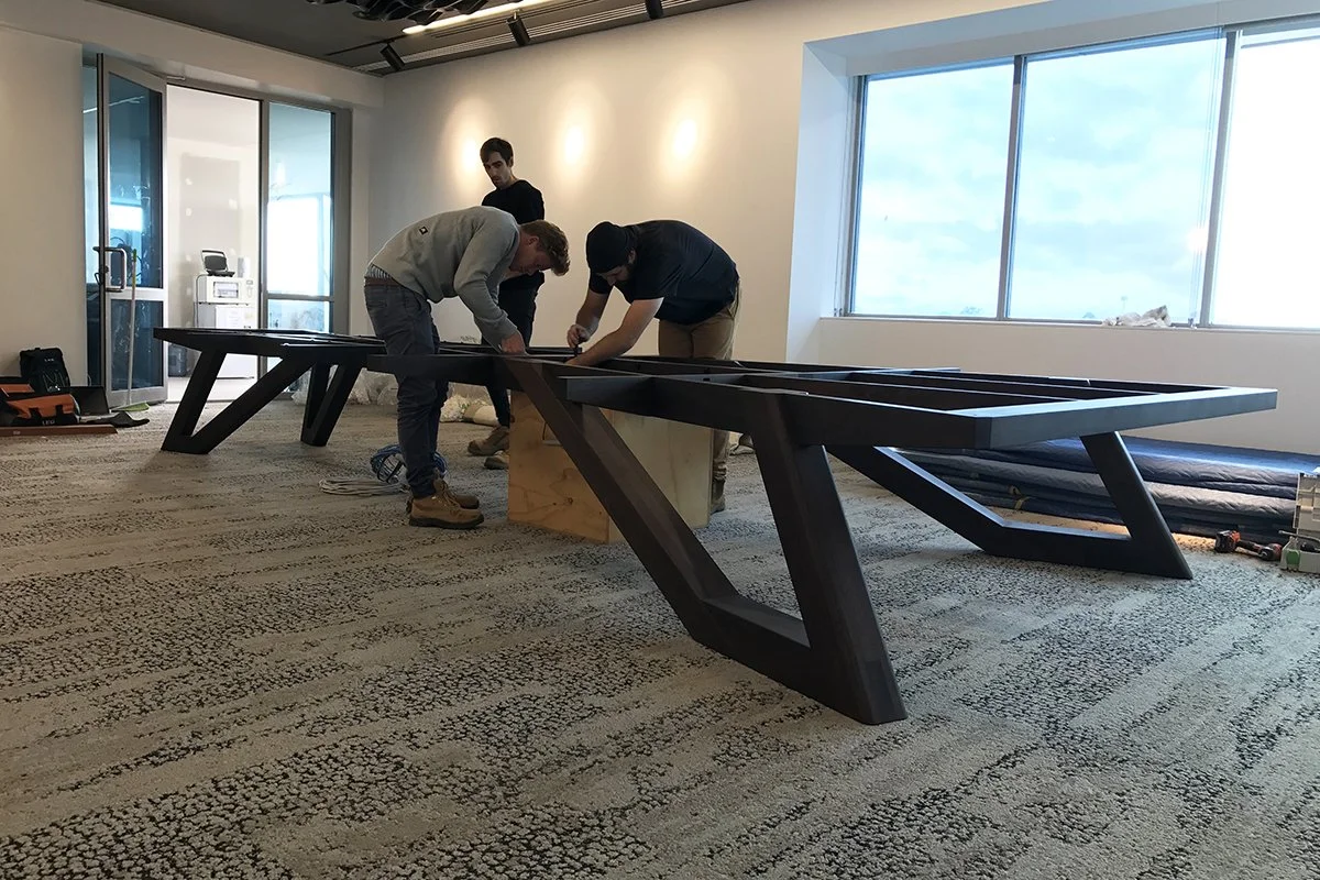 Satterley Boardroom Table in American Walnut, angular V-leg design - Nathan Day Design, installers assembling base on-site