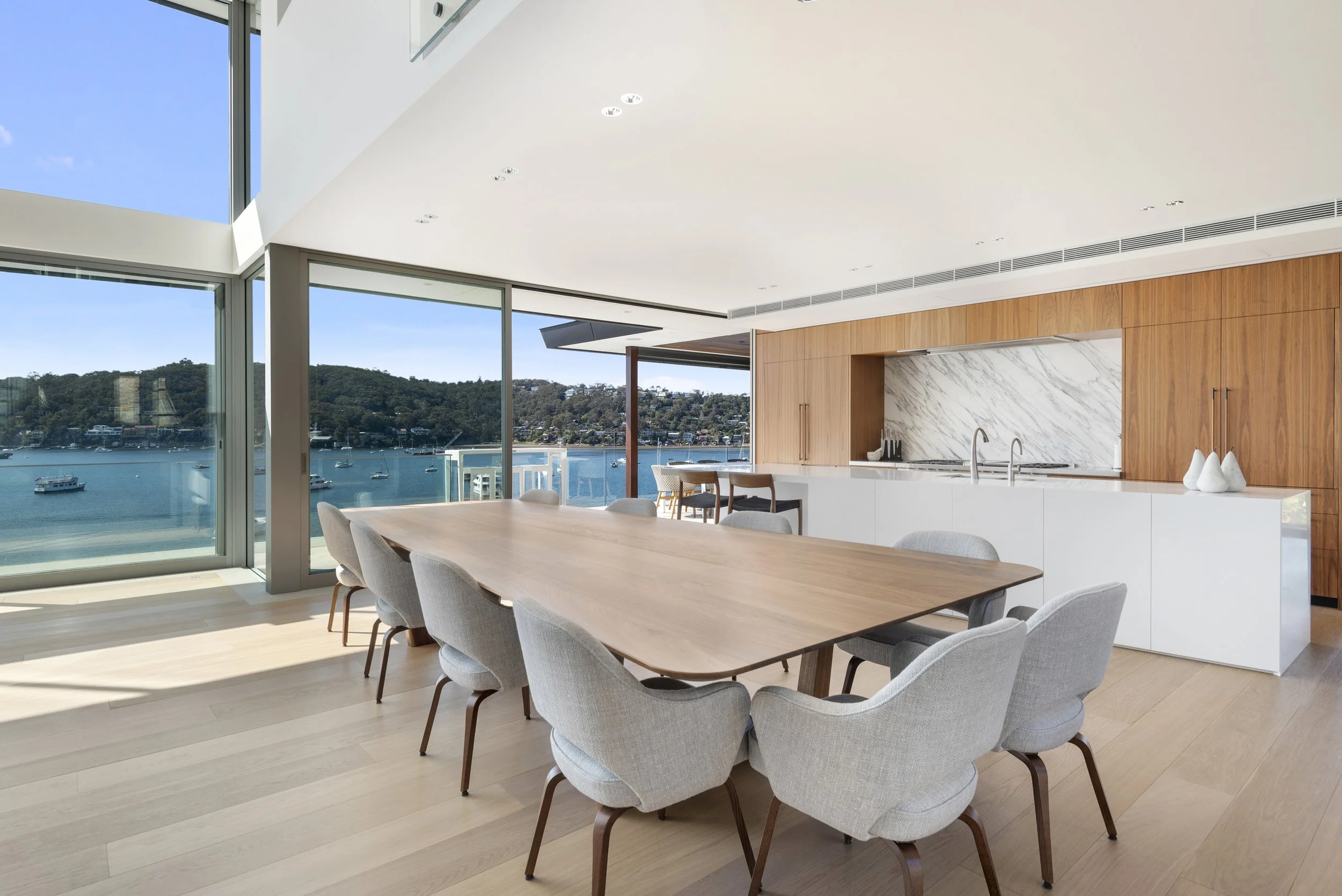 Cabarita Rd Table in Walnut set with grey upholstered chairs against a marble kitchen wall, waterfront home with bay views - bespoke furniture by Nathan Day Design