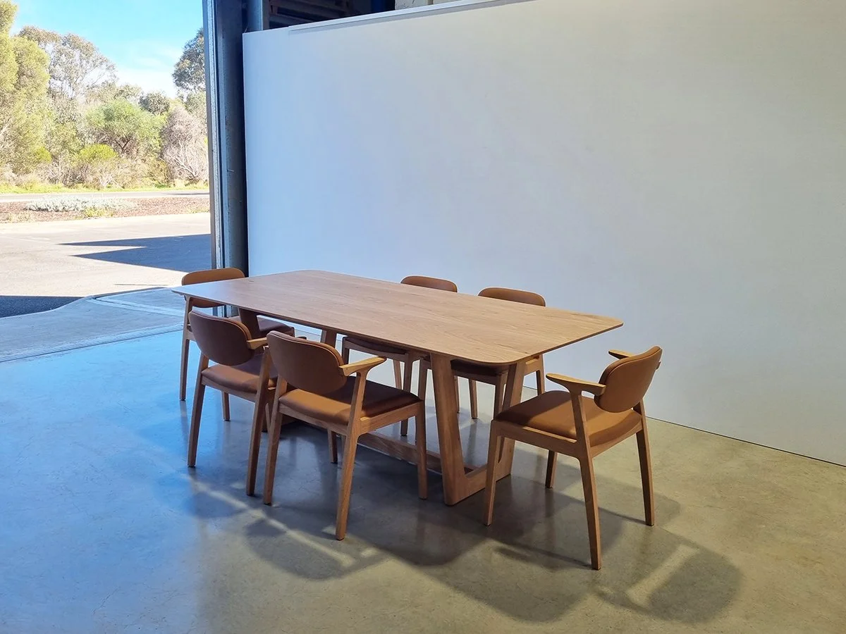 Six Kinross Chairs in tan leather set around an American Oak dining table near open workshop roller door with bushland view - bespoke furniture by Nathan Day Design