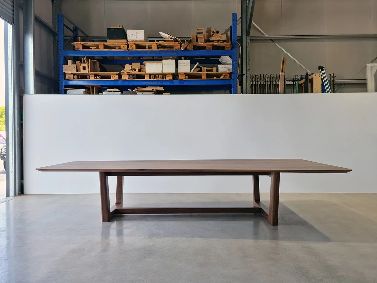 Full front-on view of Cabarita Rd Table in American Walnut showing the wide tapered end and box-frame base, near workshop doorway - bespoke furniture by Nathan Day Design