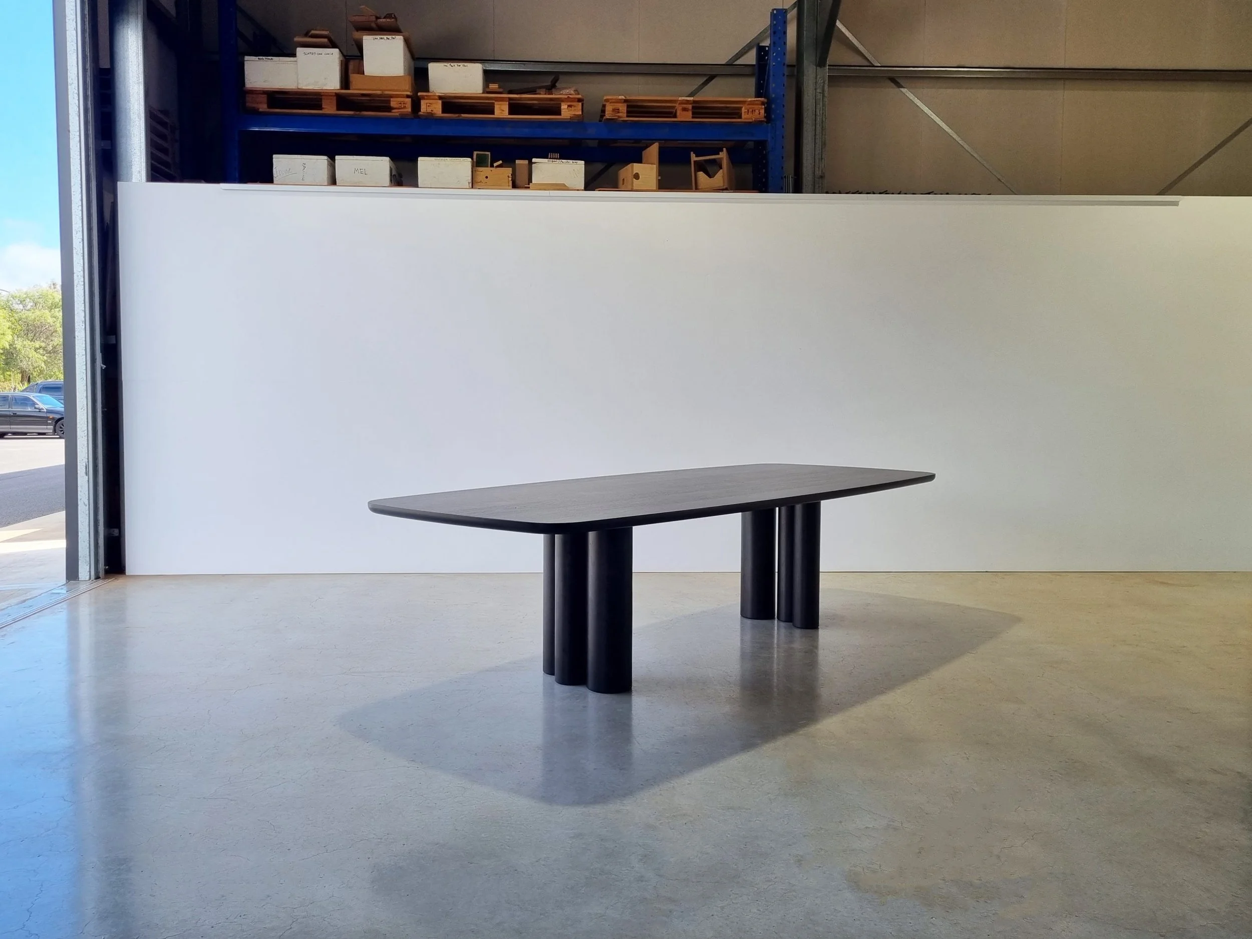 Column Table in Ebonised Walnut positioned near open workshop doorway with pallet racking behind - bespoke furniture by Nathan Day Design