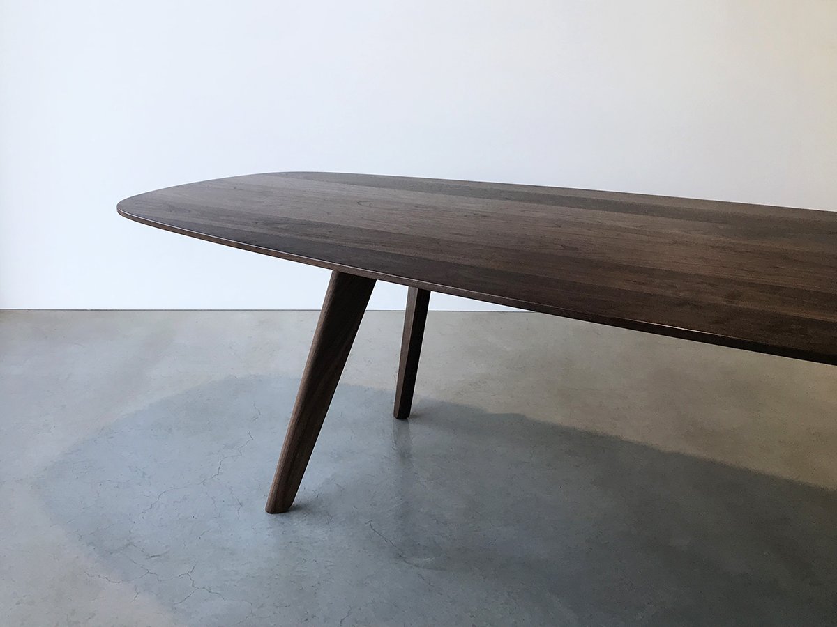 Close angled detail of Peppy Grove Table's rounded end and tapered leg pair in Walnut, showing signature bevelled edge - bespoke furniture by Nathan Day Design