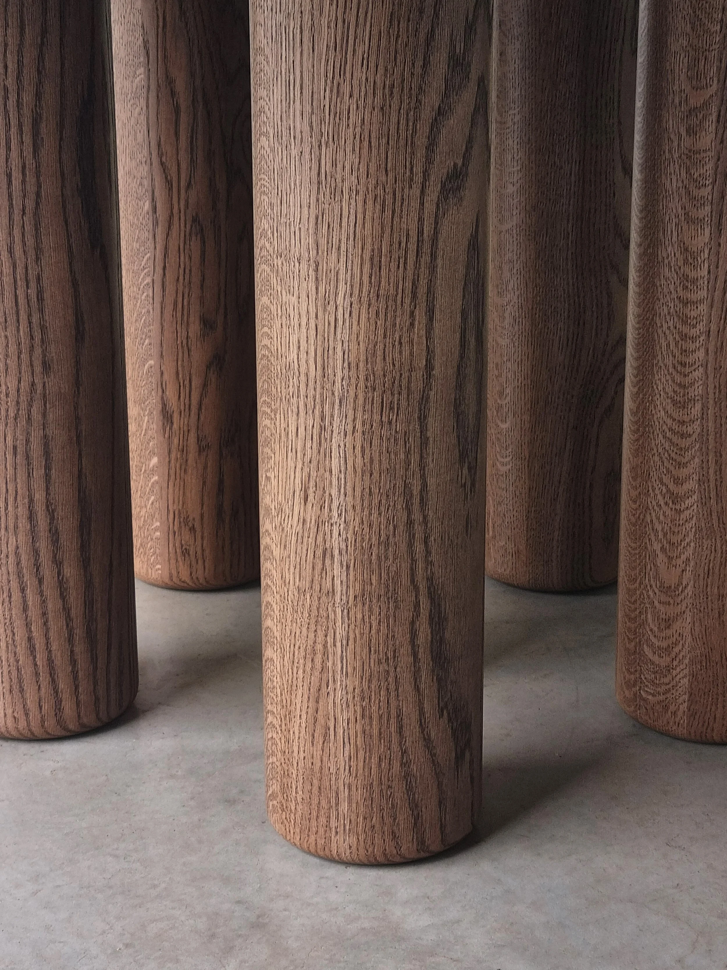 Close-up detail of Anemone Table's cylindrical column legs in tinted American Oak, showing rich timber grain - bespoke furniture by Nathan Day Design