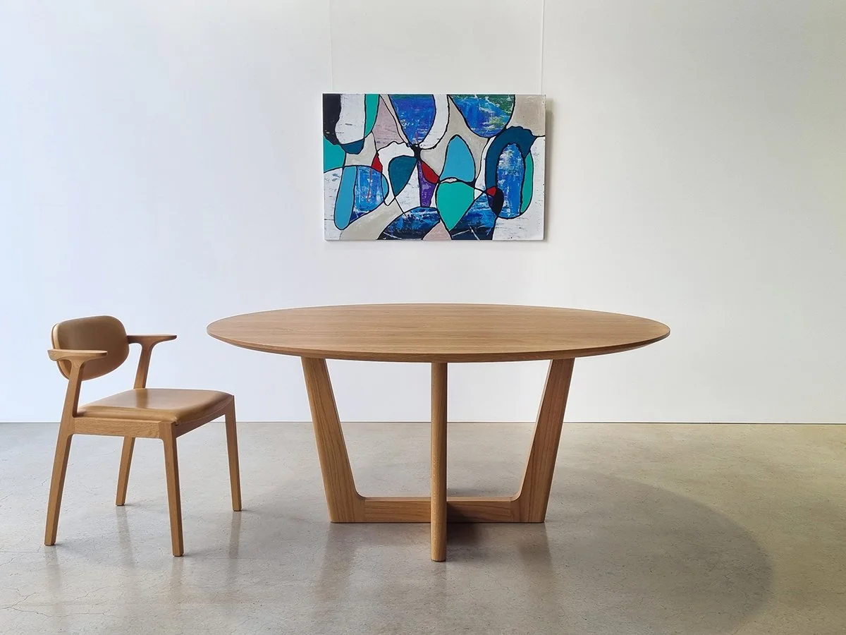 Round Botanical Table in American Oak with cross-leg base, styled with tan leather chair and abstract artwork - bespoke furniture by Nathan Day Design