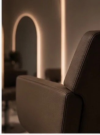 Close-up of a brown leather salon or barber chair in a modern interior with warm lighting and an arched mirror in the background.