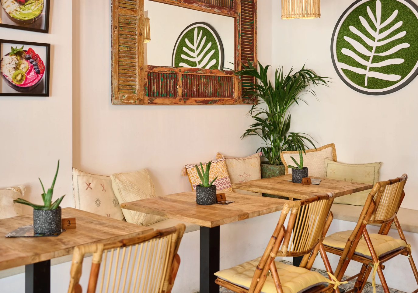 A cozy Plant Shack interior with wooden tables, rattan chairs with yellow cushions, and decorative pillows on a bench against the wall.