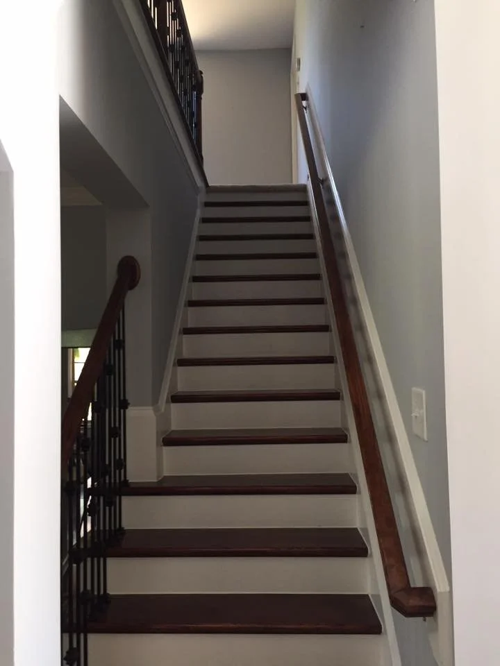 Interior view of a staircase with dark wooden steps, white risers, and wooden handrails on both sides, leading to an upper floor.