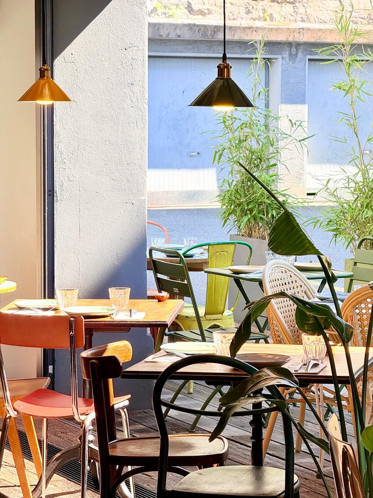 Intérieur du restaurant Yada : suspensions en laiton, chaises colorées et plantes vertes