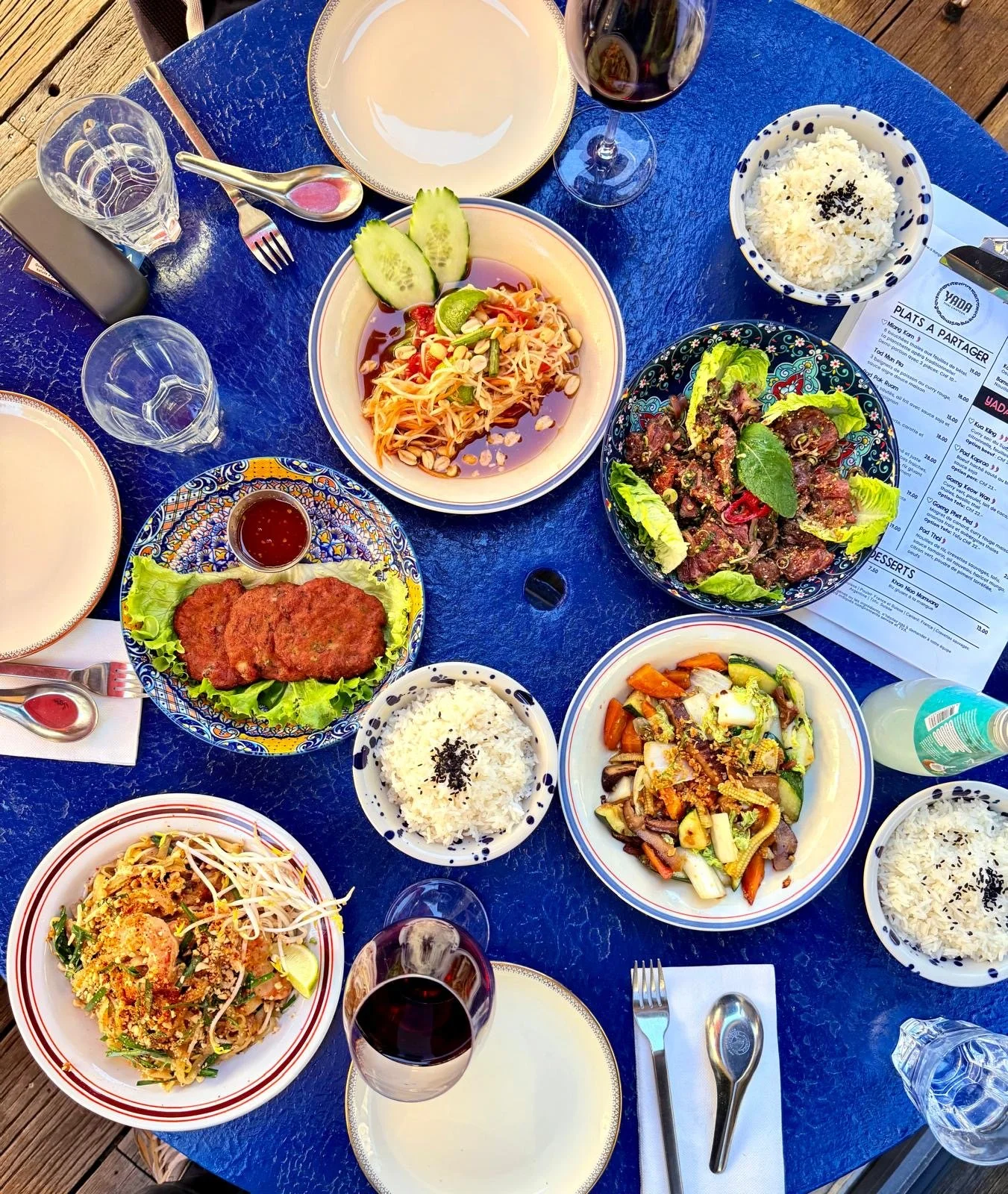 Table de plats thaïs à partager vue du dessus : salade de papaye, beignets de poisson, boeuf mariné saisi, riz et légumes sautés