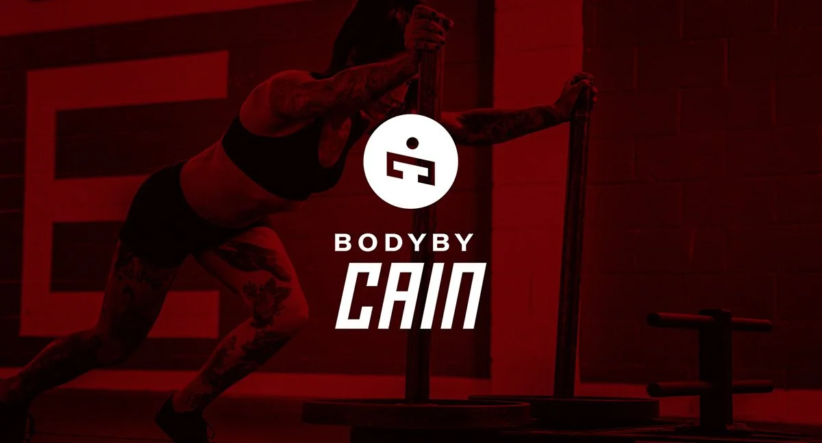 A woman with tattoos performing a workout with a sled push in a gym with red lighting, promotional text for 'Body by Cam'.