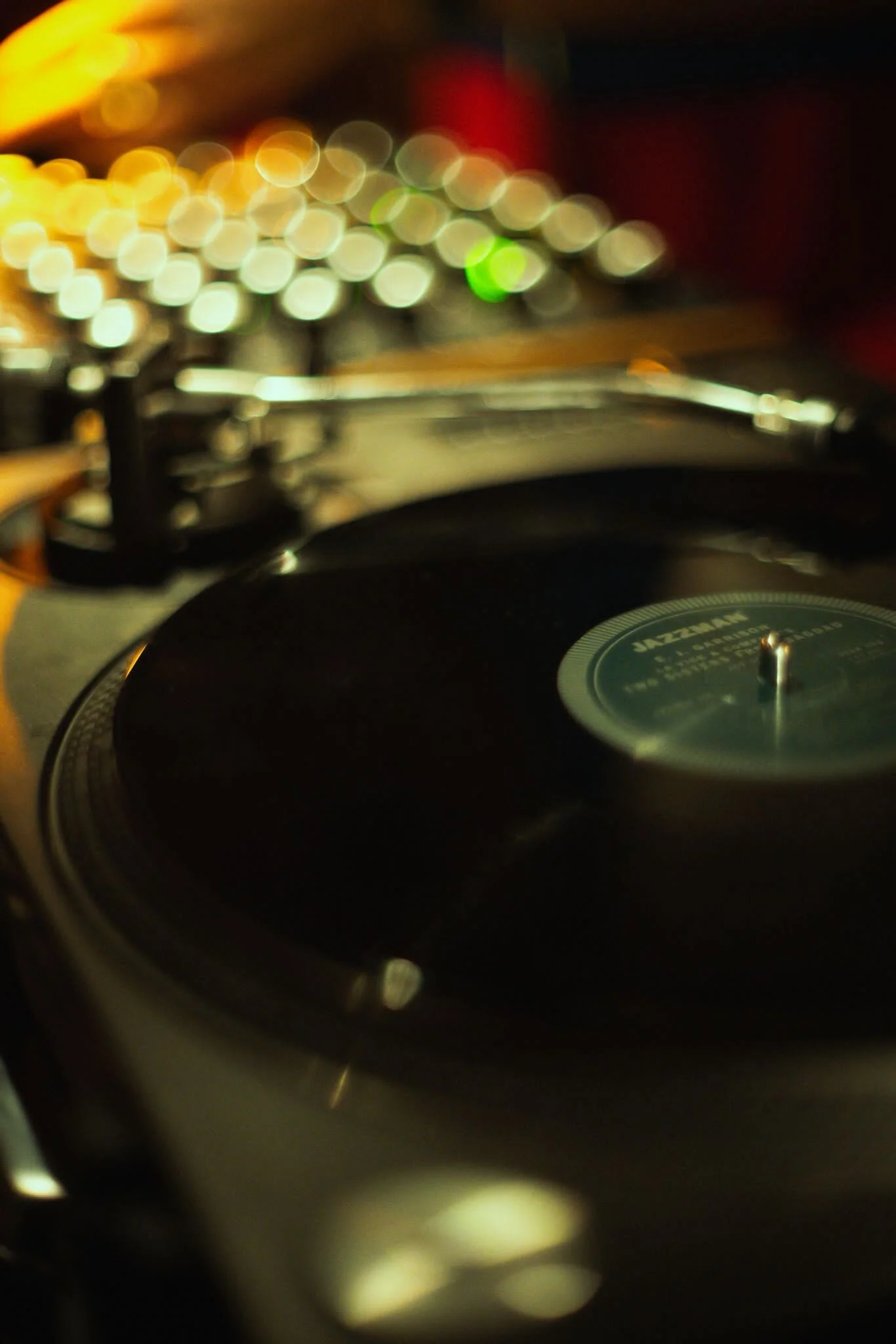 Close-up of a turntable or record player with a spinning vinyl record, blurred lights in the background.