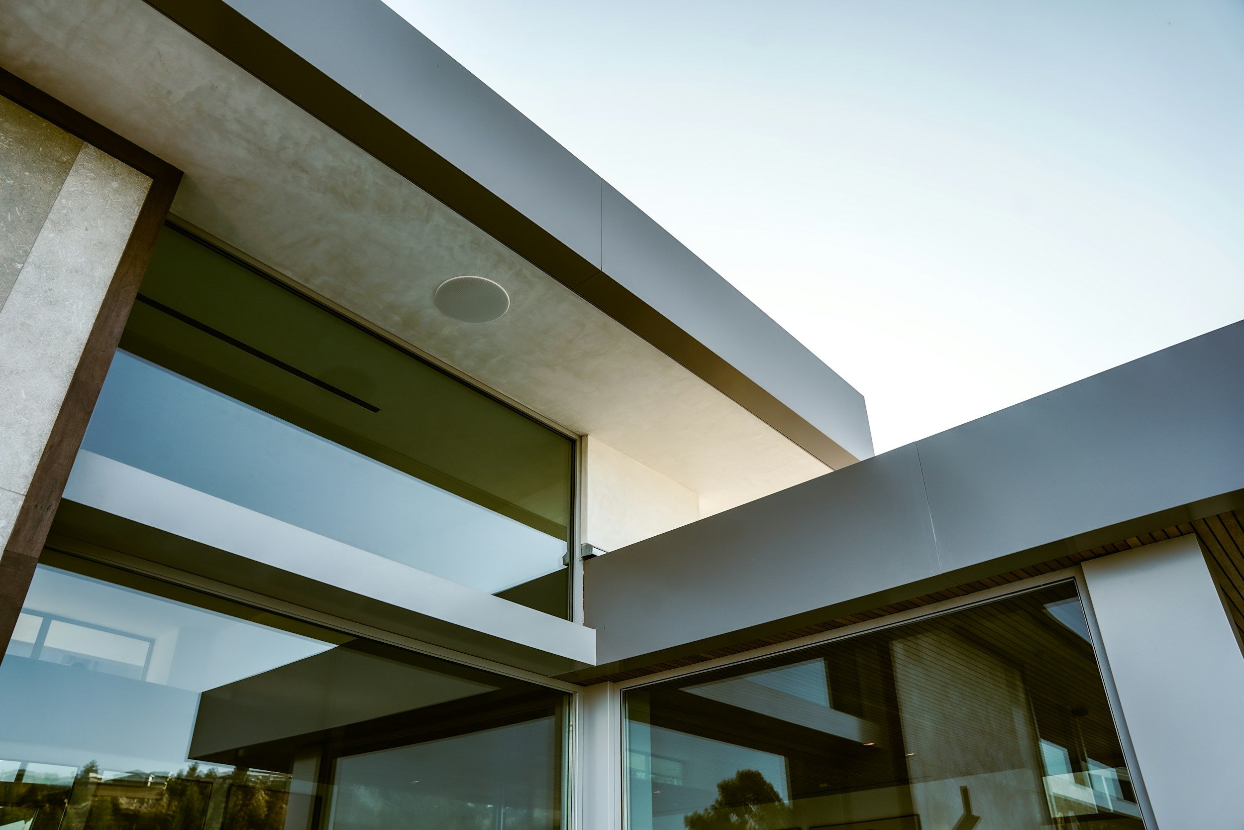 Modern building with large glass windows and white overhangs, clear sky in background. With in-ceiling speakers.
