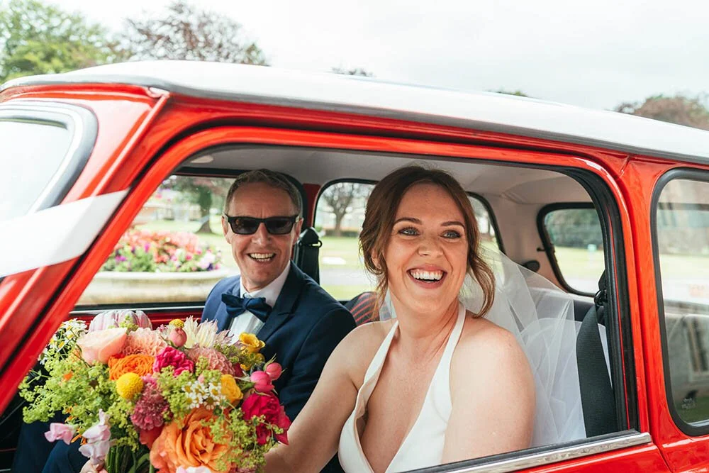 Happy bride and her father arriving at Hensol Castle in a vintage red mini car, candid moment of them looking out of the window smiling before the wedding ceremony