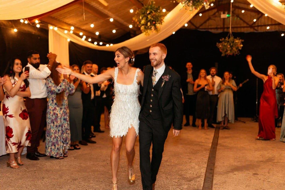 Sparkford Hall wedding night couples entrance into the rustic barn in Yeovil. Excited happy wedding photo of the newlyweds surrounded by cheering guests.