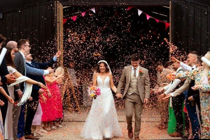 Confetti photography as newlywed couple exit the black barn at the Wholehouse venue in Talgarth, Brecon. Bride and groom walking through a tunnel of confetti being thrown by wedding guests. 