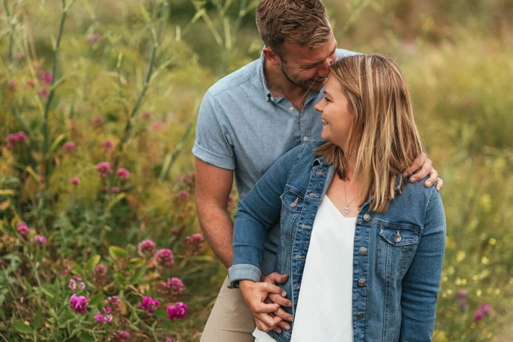 Pre wedding shoot at Port Einon bay amongst the long grass is a happy engaged couple laughing to each other.