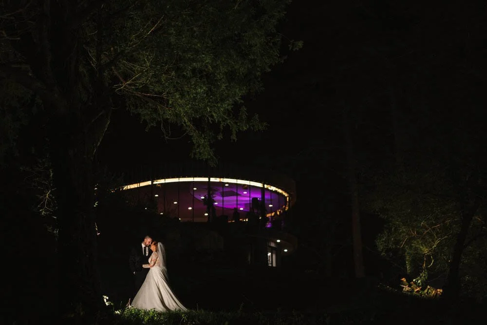Wedding couple at night outside the glass room of Fairyhill, lit up after their wedding ceremony in the forestry