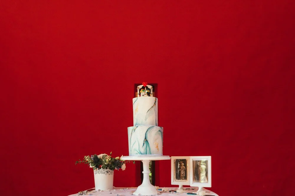 Two tier wedding cake against red wall. 