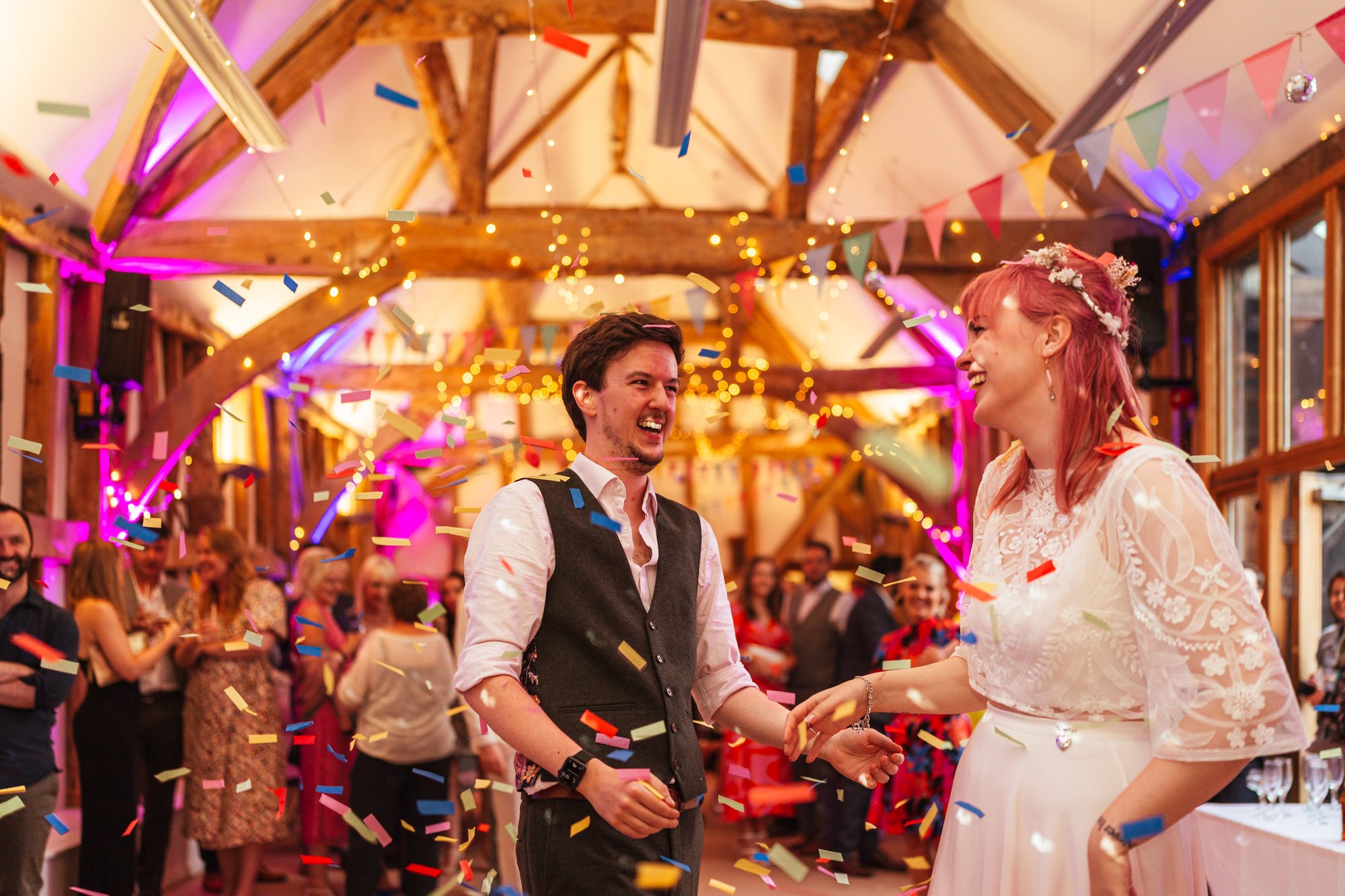 Newlywed bride and groom dancing on the dancefloor at Earth Trust Oxfordshire, confetti flying everywhere from a confetti cannon. The couple are happy and laughing.