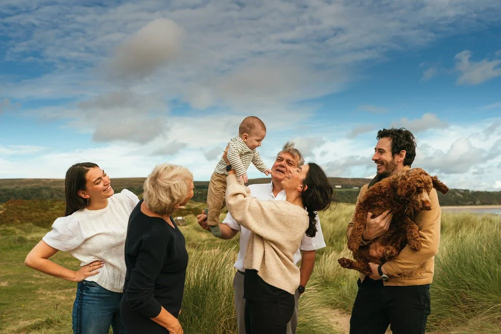 Family having fun whilst their family photoshoot is underway in the sand dunes at Oxwich beach. A blue sky background.