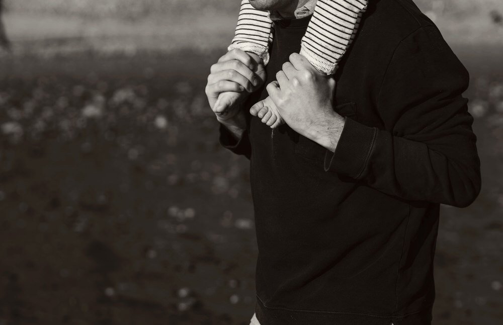 A young child's feet being held in the hands of his dad on a beach in Swansea.