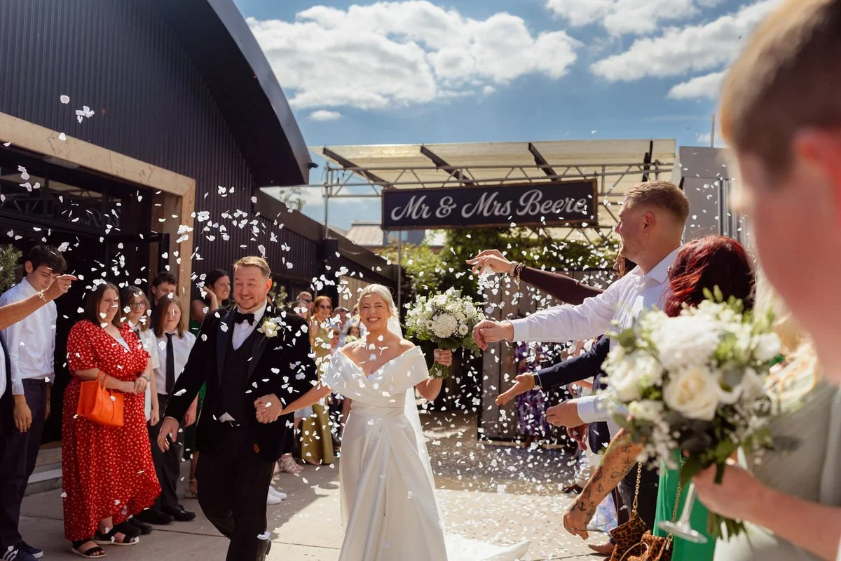 Wedding confetti throwing scene outside the Shack Revolution in Hereford. Happy couple, bride holding her flowers, guests throwing confetti from either side of the couple