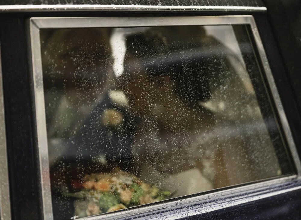 Raindrops falling down a wedding car window, the bride and father inside out of focus.